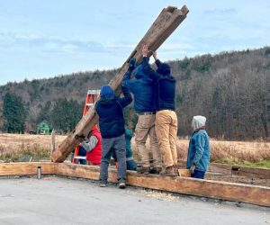 Timber framers lift a wooden beam into place